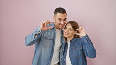 Kot gömlekli güzel bir çift parmakları küçük boyda pembe izole edilmiş arka planda duran bir işaret veriyorlar. Ölçülü aşk kavramı.