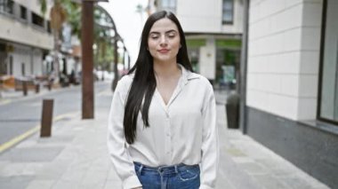 Şehir caddesinde kollarını kavuşturmuş kendine güvenen genç bir İspanyol kadın..