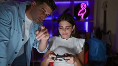 Neon ışıklı bir oyun odasında odaklanmış bir kadın ve yardımcı bir erkek geceleri yoğun bir video oyunu seansına katılıyorlar..