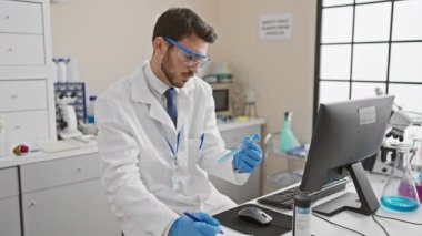 İspanyol bilim adamı modern bir laboratuvar ortamında bilgisayar ve laboratuvar ekipmanı kullanıyor..