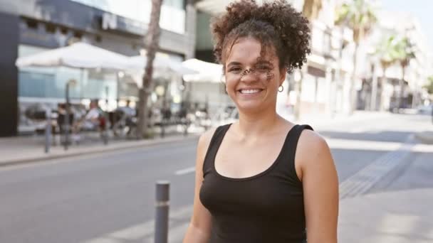 一个满头卷曲的快乐的年轻女子在阳光普照的城市街道上反射着肌肉 流露出自信和活力 — 图库视频影像