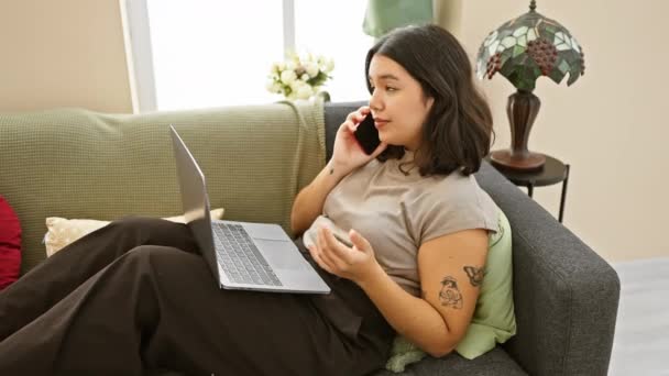穿着休闲装的西班牙女人在家里用笔记本电脑和智能手机交谈 描绘了室内轻松而现代的生活方式 — 图库视频影像