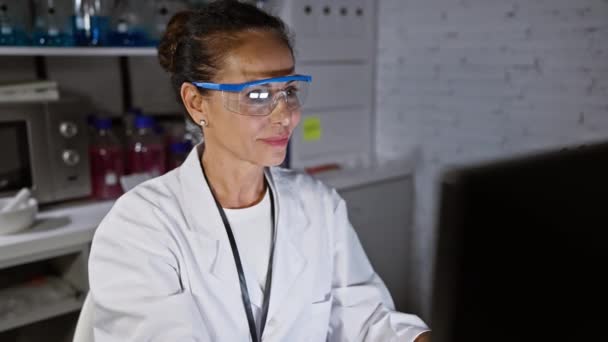 快乐的中年惊慌失措的女科学家 戴着安全眼镜 一如既往的友善 在实验室的电脑前给这个古老的 标志打手势 象征着成功和积极向上 — 图库视频影像