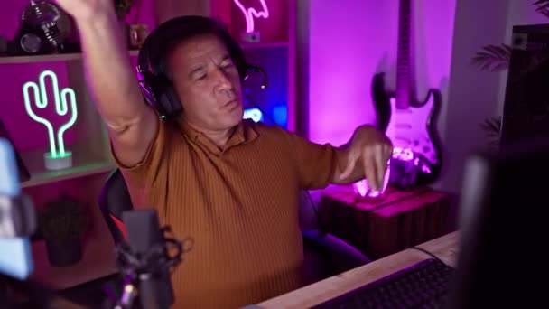 一个拿着耳机的中年男人在家里一个霓虹灯点亮的游戏室里跳舞 表达着喜悦和兴奋 — 图库视频影像