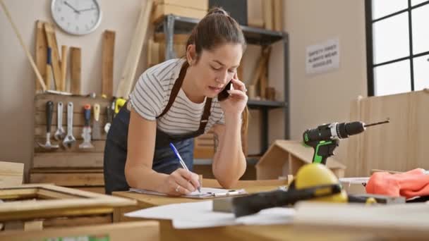 Fokuseret Kvinde Multitasking Tømrerværksted Taler Telefon Skrive Noter Omgivet Værktøjer – Stock-video