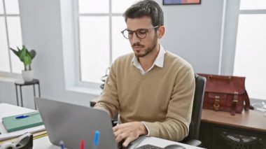 Gözlüklü ve sakallı düşünceli genç bir adam modern bir ofiste çalışıyor..