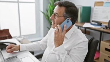 Modern ofis ortamında akıllı telefon kullanan gözlüklü olgun bir işadamı.