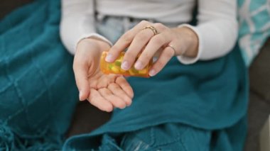 Evde genç bir kadın eline şişeden ilaç dolduruyor. Sağlık sigortası ya da ilaç tedavisini gösteriyor..