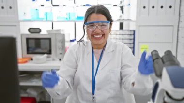 Heyecanlı genç İspanyol bilim kadını laboratuarda zaferini kutluyor! Gururlu ve sevinçten bağıran muhteşem kadın, güvenlik gözlüğü takarak kollarını kaldırıyor.