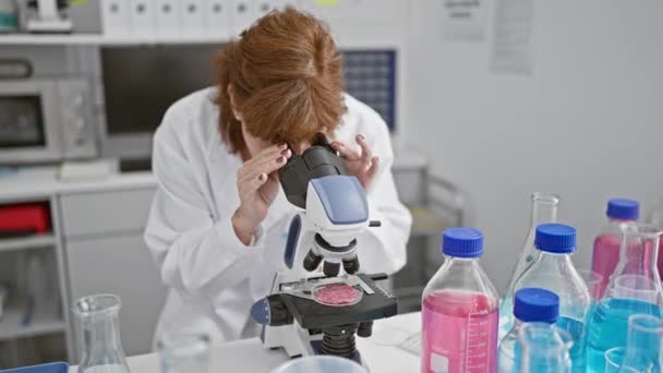 一位面带微笑的女科学家在设备齐全的实验室环境中 在显微镜下检查标本 展示研究和专门知识 — 图库视频影像
