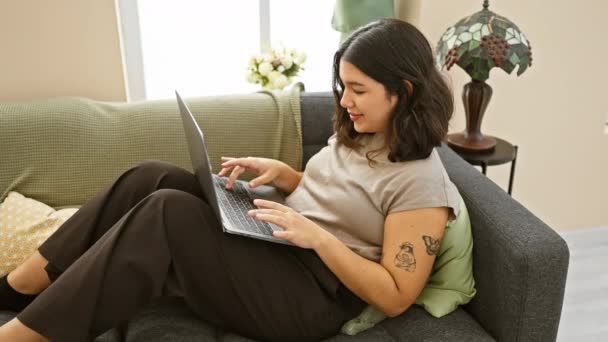 西班牙裔年轻女性带着笔记本电脑在家里的沙发上放松 散发出随意的舒适和现代生活的气息 — 图库视频影像