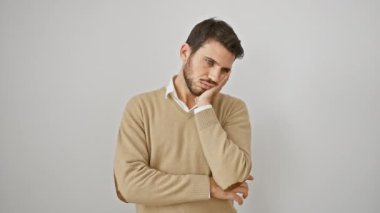 Genç, sakallı, sıkıntılı ve stresli bir İspanyol 'un portresi. Ayakta duruyor, kolları çapraz, süveter giyiyor. Yorgun görünüyor, depresyon sorunlarını beyaz, soyutlanmış bir arka planda düşünüyor..