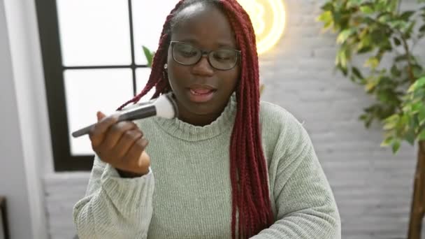 Afroamerykanka Nosząca Okulary Nakładające Makijaż Pędzlem Pomieszczeniach Pokazując Piękno Osobistą — Wideo stockowe