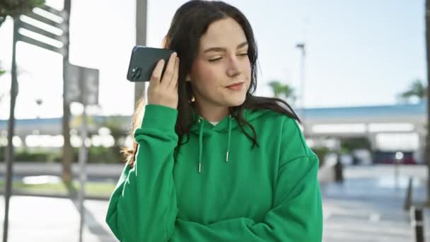 Mujer Joven Atractiva Con Capucha Verde Sonríe Mientras Escucha Mensaje — Vídeo de stock