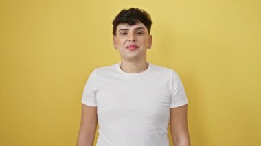 Neşeli genç adam, kendinden emin ve başarılı, başarıyı kutlayan, kazanan bir gülümseme saçan! Tek başına duruyor, beyaz bir tişört giyiyor ve parlak sarı bir arka plana yaslanıyor..