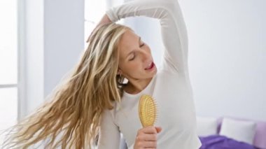Neşeli genç bir kadın, parlak bir yatak odası ortamında saç fırçasını mikrofon olarak kullanarak şarkı söylüyor. Evde neşeli ve kaygısız bir an sergiliyor..