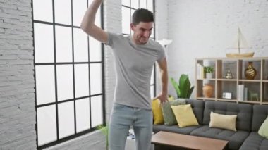 Genç İspanyol adam modern bir salonda dans ederken akıllı telefon kullanıyor, neşe ve eğlence ifade ediyor..