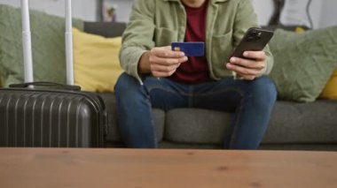 Kredi kartı ve akıllı telefonu olan düşünceli bir adam oturma odasındaki bavulların yanındaki koltukta oturur, seyahat ve mali konuları düşünür..
