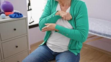 Rehabilitasyon kliniğinde dirseğine dokunan acı çeken olgun bir kadın..