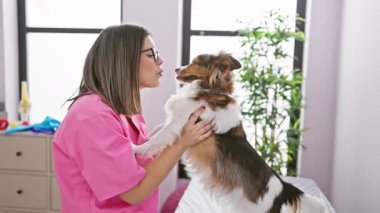Pembe çalılık içinde gülümseyen genç bir kadın parlak bir veteriner kliniğinde mutlu bir köpek tutuyor..