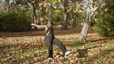 Güneşli bir parkta sonbahar yapraklarıyla oynayan gülümseyen genç kadın, neşe ve sonbaharın güzelliğinin somutlaştırıcısı..