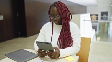 Örgülü Afrikalı kadın modern ofiste tablet kullanıyor, teknoloji, iş ve çeşitlilik tasvir ediyor..