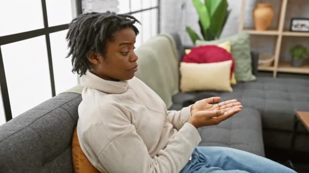 ドレッドロックと興奮した若い黒人女性は 快適に彼女の居心地の良いホームソファーに座って 広告を提示しながら静かに指摘しました コピースペースに向かって ジェスチャーが口を開いて 幸せが放射します — ストック動画