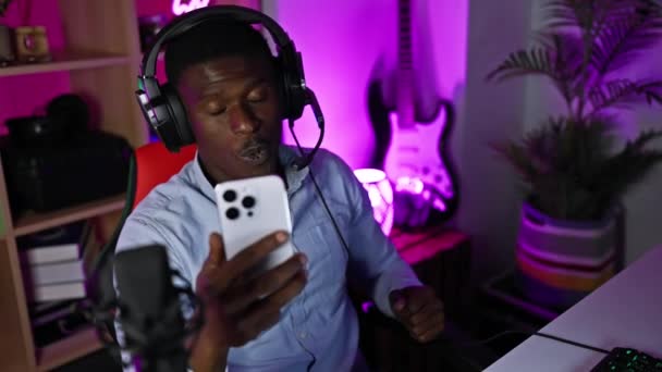 Gece Renkli Oyun Odasında Kulaklıklı Afrikalı Adam Akıllı Telefon Kullanıyor — Stok video
