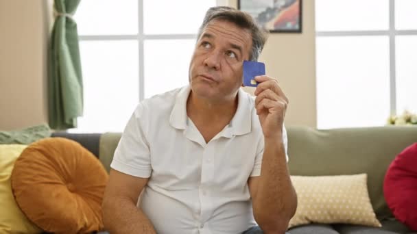 一个头脑清醒的中年男人拿着信用卡 在他舒适的客厅里想着开支 — 图库视频影像