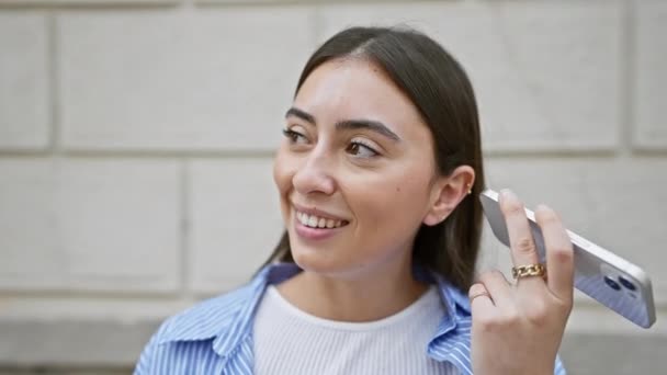 スマートフォンで話す若いヒスパニック系女性を笑顔で都市環境で気軽に服を着た — ストック動画
