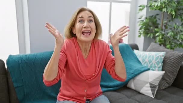 Medelålders Blond Kvinna Sitter Soffan Firar Seger Med Glada Leende — Stockvideo