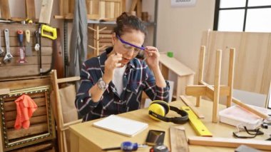 Yorgun İspanyol kadın iyi donanımlı bir marangoz atölyesinde güvenlik gözlüklerini çıkarıyor.