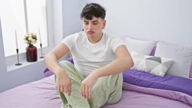 Sıkıntılı bir genç adam yatak odasında bir yatakta oturuyor, kafasını endişeli bir şekilde tutuyor..