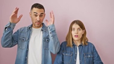 Şokta olan güzel bir çift, pembe izole edilmiş arka planda çılgın bir şaşkınlık içinde duruyor. Korkmuş ve şaşırmış, elleri başının üstünde, ağzı açık aşk ve stresi kot pantolon giymiş bir ifadeyle birleştirmiş.. 