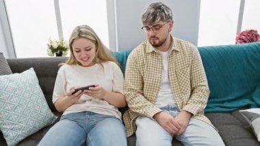 Samimi bir oturma odasındaki kanepede oturan ilgisiz bir adamın yanında akıllı telefon kullanan bir kadın.