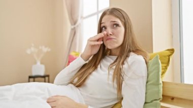 Pijamalı, stresli bir sarışındı. Yatak odasında yalnız bir şekilde oturan endişeli ve sinirli genç bir kadının ağlama ifadesi.