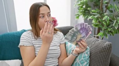 Güzel esmer bir kadın, mavi gözleri şoke olmuş, ağzı ve elleri evde şaşkınlıkla kaplı, Filipinli peso banknotlarını kavramış.