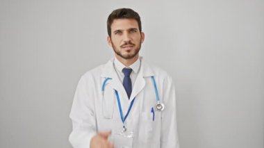 Neşeli genç İspanyol bir adam, bir gözünü elinle kapayan bir doktor, steteskop takıyor, izole edilmiş beyaz arka planda güvenle gülümsüyor, dikizleme hareketini mükemmelleştiriyor.!