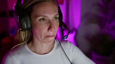 Gece loş aydınlatılmış bir oyun odasında kulaklık takan düşünceli genç bir kadın sakin bir ortam yayıyor..