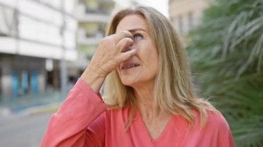 Pembe tişörtlü orta yaşlı bir kadın şehir sokaklarında parlak güneş ışığında şaşı bir şekilde günlük bir şehir manzarasını canlandırıyor..