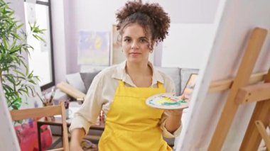 Kıvırcık saçlı, kendine güveni tam bir İspanyol sanatçı. Stüdyoda parmakları küçük boy işareti yapıyor.