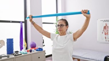 Olgun kadın fizik tedavi kliniğinde direnç bandıyla egzersiz yapıyor.