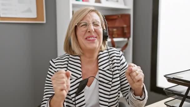快乐的中年女性 戴着眼镜和耳机 在办公室里庆祝 — 图库视频影像