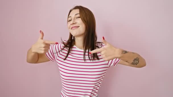 スマイリー ストライプTシャツに自信を持って若いブルネットガール 誇らしげに孤立したピンクの背景の上に自分自身を指す 幸せの肖像画 カジュアルな成功と偉大な自己尊敬 — ストック動画