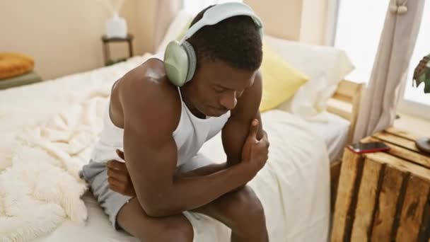 Afroamerikaner Mit Kopfhörern Sitzt Vor Schmerzen Hause Bett — Stockvideo