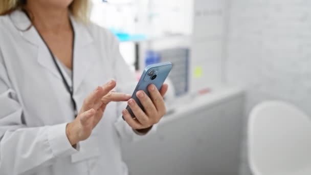 在现代实验室里 一位穿着白大褂的成熟女人一边笑一边用智能手机描绘医疗保健技术 — 图库视频影像