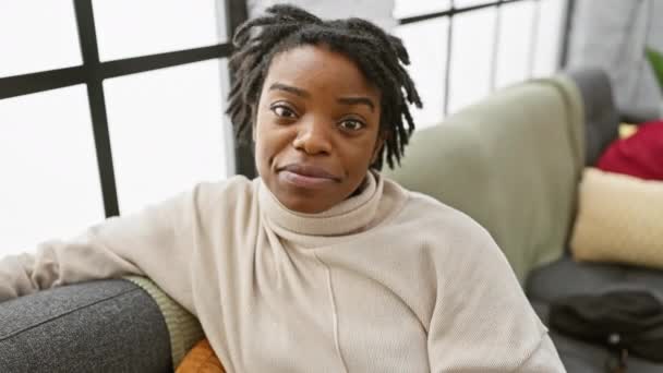 快乐的年轻黑人女人 留着可怕的头发 坐在舒适的沙发上 用手指在喜庆的脸上做一个和平的象征 露出胜利的微笑 — 图库视频影像