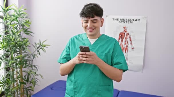 在诊所的检查室 靠近解剖海报和植物的地方 用智能手机在灌木丛中微笑的年轻人 — 图库视频影像
