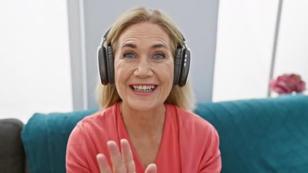 Lächelnde Blonde Frau Mittleren Alters Die Hause Kopfhörer Trägt Und — Stockvideo