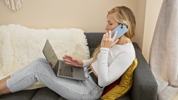 一个年轻的女人带着电话和笔记本电脑 在舒适的客厅里忙着多项任务 描绘着连接和现代的家庭生活 — 图库视频影像
